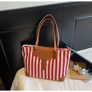 Detail of red and white striped canvas tote bag with brown leather handles and metal lock