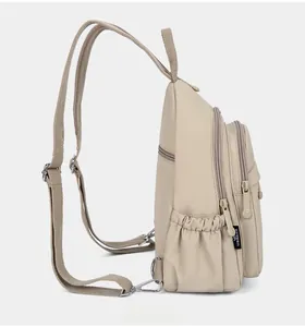 Side view of beige nylon backpack showing multiple zipper layers and side pockets