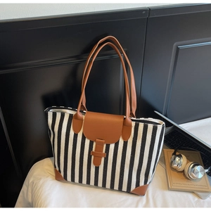 Detail of striped canvas tote bag with brown leather trim styled on a white bed