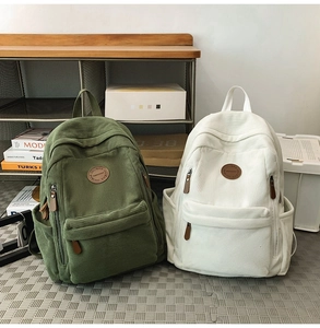 Detail of olive green and off-white corduroy backpacks with JULIBAG logo on textured mat