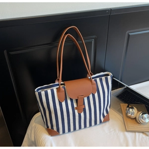 Blue and white striped canvas tote bag with brown leather handles on a white bed