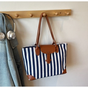 Detail of striped canvas tote bag hanging with leather strap and flap closure