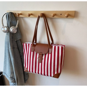 Detail of red and white striped canvas tote bag with brown leather handles hanging on a rack
