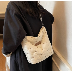 Détail d'un sac cabas matelassé crème avec broderie nœud marron et étiquette cuir
