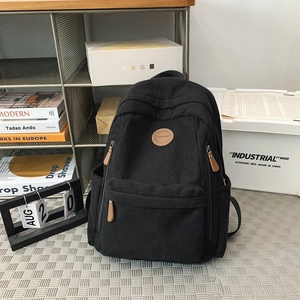Detail of black corduroy backpack featuring a round leather logo and multiple pockets