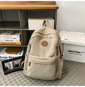 Detail of beige corduroy backpack with front pocket and circular logo in a retro setting