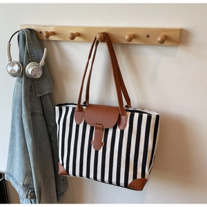 Detail of striped tote bag with brown leather accents hanging on a wooden rack