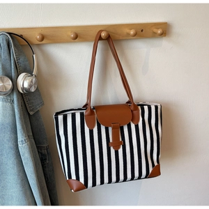 Detail of a large vertical striped canvas tote bag with brown leather handles and base