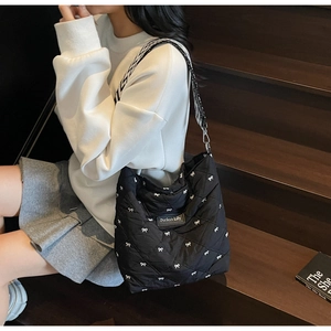 Détail d'un sac bandoulière noir matelassé avec nœuds blancs et large bandoulière
