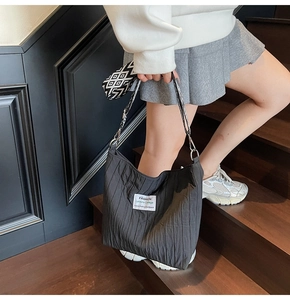 Détail du sac cabas plissé noir avec étiquette blanche sur des marches en bois