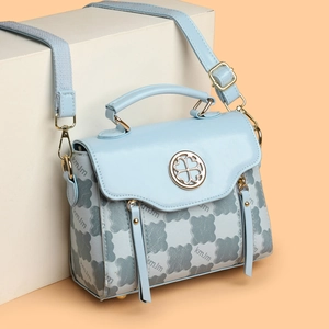 Light blue plaid handbag with clover logo and adjustable strap on a warm background