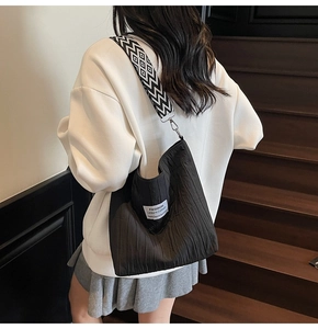 Détail du sac cabas texturé noir avec une large bandoulière rayée et une étiquette tissée chic