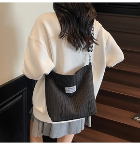 Détail du sac bandoulière noir plissé avec une sangle géométrique portée par un modèle