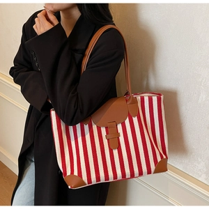 Detail of red and white striped tote bag with brown leather handles worn by a model