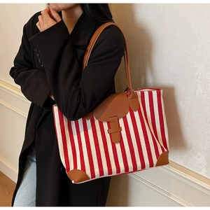 Detailed side view of a large red and white striped canvas tote bag with brown leather trim