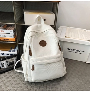 Detailed view of white corduroy backpack with leather logo and textured fabric finish