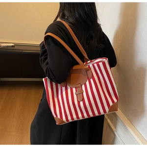 Detail of red and white striped canvas tote bag with brown leather handles and accents