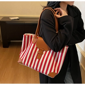 Side view of large red and white striped canvas tote bag with brown leather straps and flap