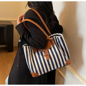 Large striped canvas tote bag with brown leather handles worn by a woman for daily commute