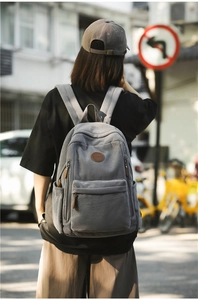 Close-up of gray corduroy backpack showing textured fabric and front leather logo detail