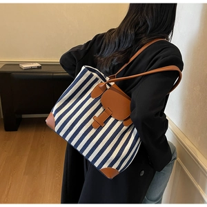 Detail of blue and white striped canvas tote bag with brown leather handles and flap