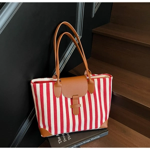 Detail of red and white striped canvas tote bag with brown leather handles and base