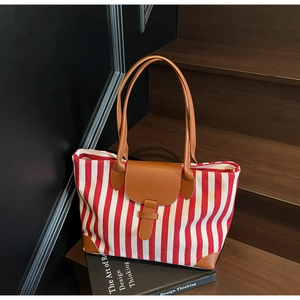 Detail of red and white striped canvas tote bag with brown leather handles on wooden stairs