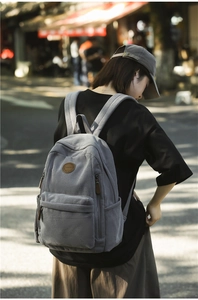 Outdoor street shot of a gray corduroy backpack with vintage logo and front pocket