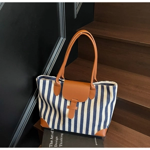 Close-up of blue and white striped tote bag with brown leather accents on wooden stairs