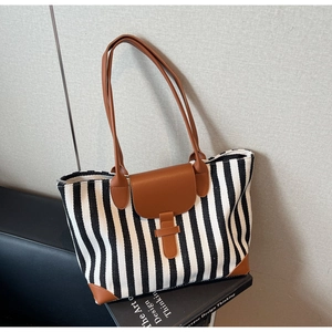 Detail of striped canvas tote bag with brown leather trim resting on a design book