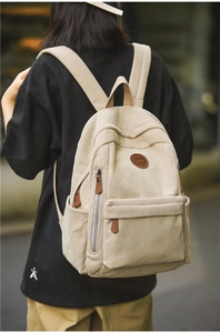 Detailed texture of beige corduroy backpack with brown leather logo and zipper pull