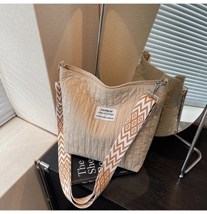 Détail du cabas en toile beige matelassée avec étiquette et bandoulière géométrique