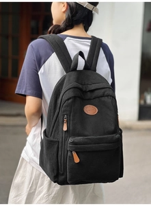 Detail of black corduroy backpack showing large capacity and brown leather logo tag