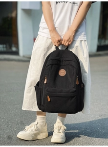 Close-up of black corduroy backpack with leather logo patch and brown zipper details
