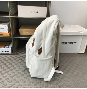 Detail of white corduroy backpack showing side pocket and brown leather zipper pull