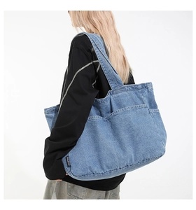 Side view of large denim tote bag worn by a model showcasing blue washed fabric texture