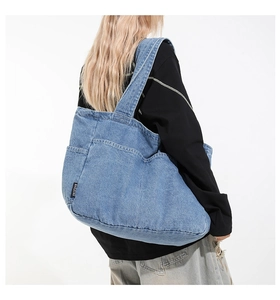 Detail of light blue denim tote bag with black logo tag and adjustable shoulder strap