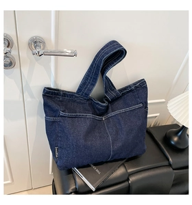 Detail of blue denim tote bag showing white contrast stitching and branded side label