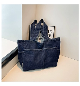 Detail of dark blue denim tote bag featuring multiple pockets and white stitching