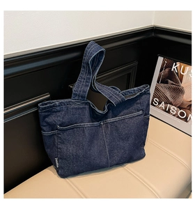 Detailed view of dark blue denim tote bag with white stitching on a beige bench