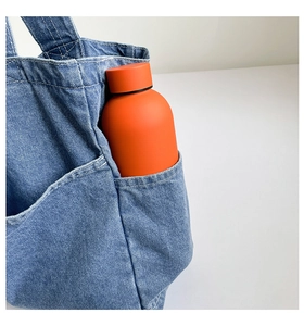 Macro view of matte orange thermos bottle placed inside a blue denim tote bag pocket