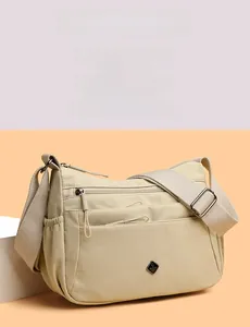Close-up of cream beige nylon crossbody bag featuring multiple zipper pockets and wide strap