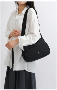 Detailed view of black nylon multi-pocket crossbody bag worn by a model in casual style