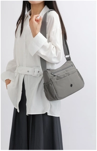 Detail view of grey nylon shoulder bag with multiple pockets and wide strap on model