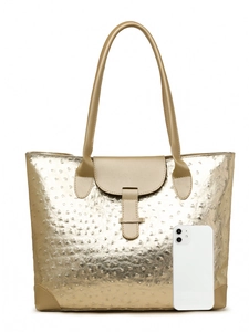 Detail of metallic gold tote bag with ostrich texture and elongated handles beside a phone