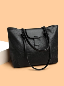 Detail view of black ostrich texture tote bag with buckle closure and sturdy base corners