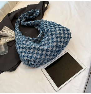 Detail of blue checkerboard denim hobo bag with fringe edges on a white fabric surface