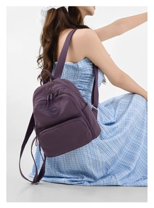 Side view of a purple nylon backpack with adjustable straps worn by a model in a dress