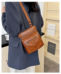 Side view of caramel brown crossbody bag with multi-layer zippers on a blue blazer