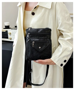 Detail of a black multi-layer crossbody phone bag with three silver zippers and metal snap